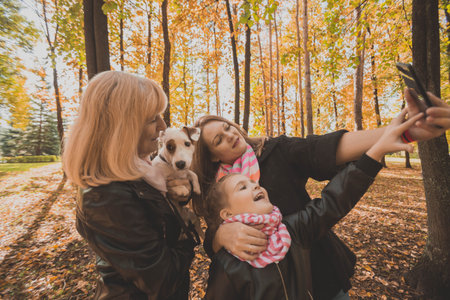 Mother, grandmother and little granddaughter with jack russell terrier dog taking selfie by smartphone outdoors in autumn nature. Family, pets and generation conceptの写真素材