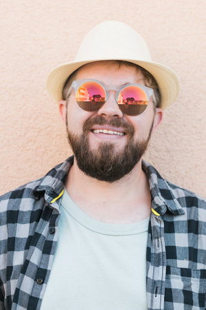 Close-up portrait millennial man wearing summer hat and sunglasses and plaid shirt smiling happy near wall - travel vacations and summer holiday conceptの写真素材