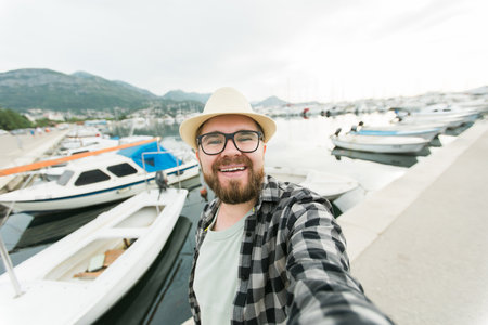 Traveller millennial man taking selfie of luxury yachts marine during sunny day - travel and videocall and blogging conceptの写真素材