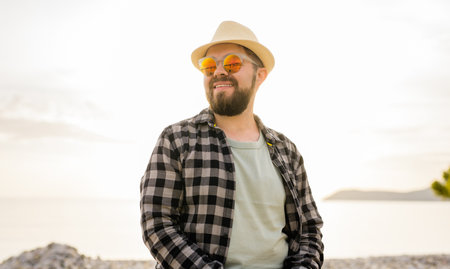 Handsome and confident. Outdoor portrait of smiling millennial man wearing hat and sunglasses on...