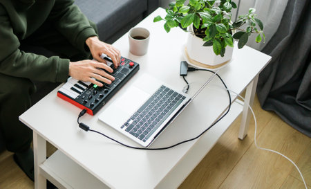Man recording electronic music track with portable midi keyboard on laptop computer in home studio. Producing and mixing music beat making and arranging audio content with professional audio devicesの写真素材