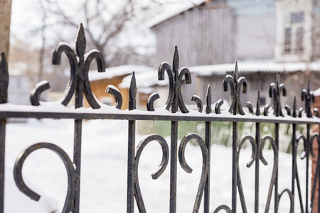Elements of ornamental ornament in a metal forged fence are covered with snow in winter seasonの写真素材