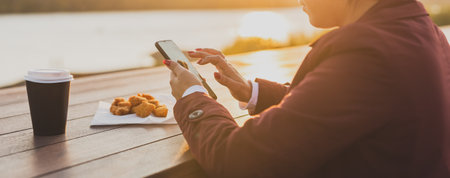 Banner muslim woman in hijab using smartphone outdoor tasty nuggets and coffee background, close up. Street food and picnic in spring morningの写真素材