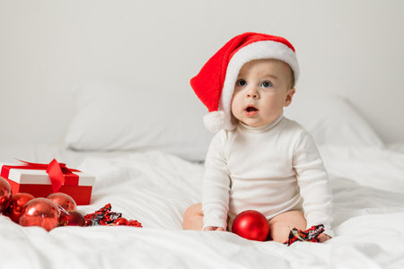Christmas Baby in Santa Hat, Child holding christmas bauble near Present Gift Box over Holiday Lights backgroundの写真素材
