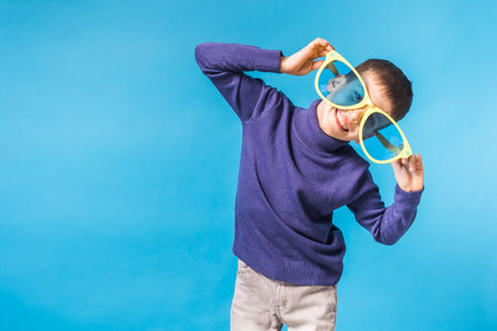 Cheerful little boy in big glasses express a surprised face isolated on blue background with copy spaceの写真素材