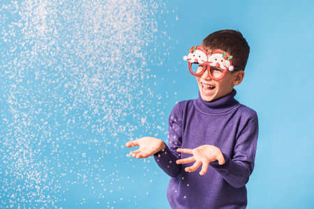 Child boy blowing snow out of his hands on blue background. Christmas and New Year holidays concept. Generation alpha and gen alpha children. Copy spaceの写真素材