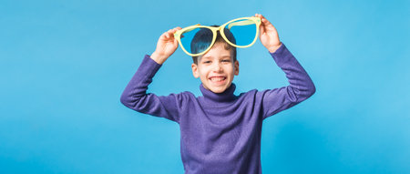 Banner Cheerful little boy generation alpha in big glasses express a surprised face isolated on blue background with copy spaceの写真素材