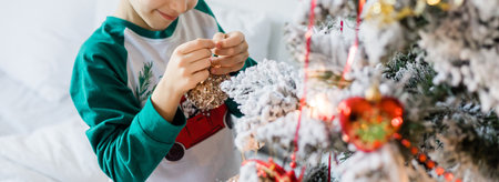 Banner Child decorates Christmas tree copy space mockup. The boy is holding a Christmas toy. Morning before christmas at home. Generation alpha and gen alpha children.の写真素材