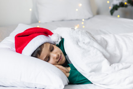 Sweet child boy sleeping in bed wearing Santa Claus hat in Christmas eveの写真素材