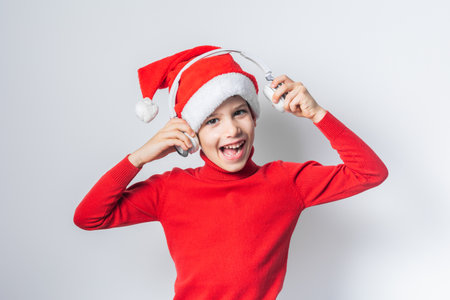 Funny child boy holds listening to Christmas music with Santa Claus hat on white background. Generation alpha and gen alpha children.の写真素材