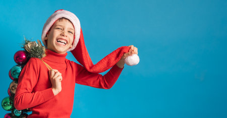 Banner cheerful child in santa hat hold christmas decorative balls on blue background, Xmas and holidays concept mockup. Generation alpha and gen alpha children.の写真素材