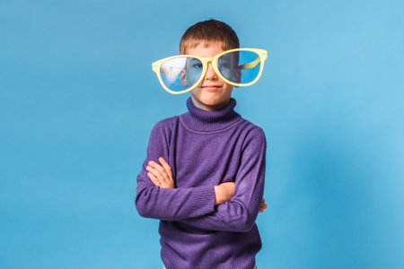 Cheerful little boy in big glasses express a surprised face isolated on blue background. Generation...