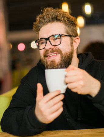 Portrait Bearded curly man smiling confident drinking coffee in restaurant or coffee shop. Millennial generation and Gen Yの写真素材