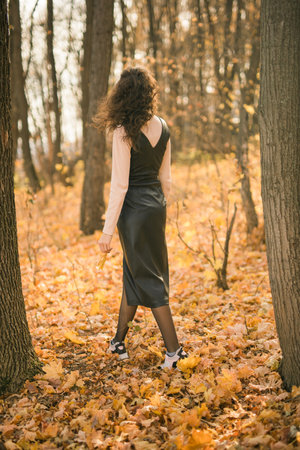 Attractive young woman walking in autumn park, happy mood and fashion style trend and curly long brown hair. Fall season and pretty female portrait copy space. Millennial generation conceptの写真素材