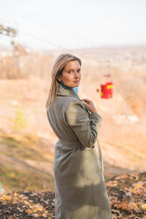Blonde woman in elegant gray coat walks in the sunny autumn season park. Generation z and gen z youth concept.の写真素材