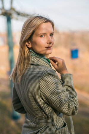 Blonde woman in elegant gray coat walks in the sunny autumn season park portrait. Generation z and gen z youth concept.の写真素材