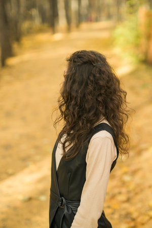 Girl in fall park back view. Woman with long curly hair. Beautiful sunlight in the forest. Hair care. Millennial Generation and youth.の写真素材