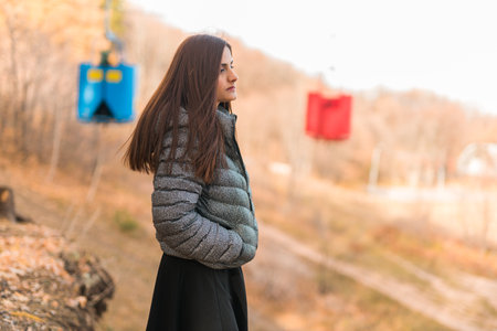 Girl in fall park against background of cable car copy space. Woman with long curly hair. Beautiful sunlight in the forest. Hair care. Generation Z gen z and youth.の写真素材