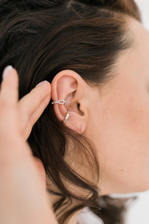 Cropped close-up shot of a young woman with asymmetrical silver ear cuffs. Female with metal ear...