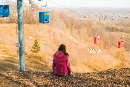 Back view of a girl woman resting on autumn park in fall season and look at the cable car....