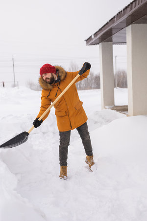 Young man clearing snow in his backyard village house with shovel. Remove snow from the sidewalk.の写真素材