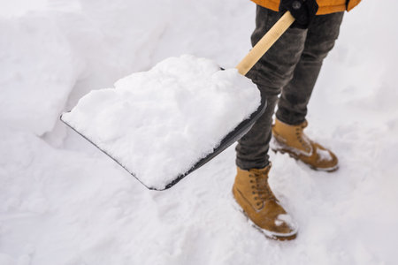 Close-up man cleaning snow from sidewalk and using snow shovel. Winter seasonの写真素材