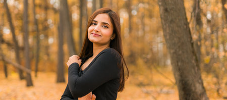 Banner portrait of diversity young beautiful confident Indian Asian woman in black dress in fall outdoor copy space mockup. Happy and natural smiling female. Generation z and gen z youth conceptの写真素材