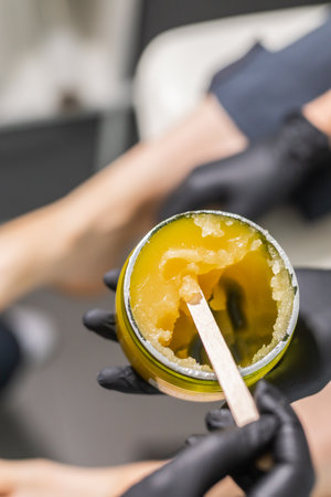 Orange body scrub with sugar and oil in glass jar in female hand. Homemade cosmetic for peeling and spa care. Copy space and empty place for advertisingの写真素材