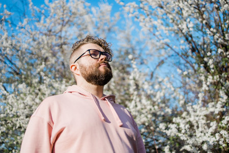 Handsome man outdoors portrait on background cherry blossoms or apple blossoms and blue spring sky. Millennial generation guy and new masculinity conceptの写真素材