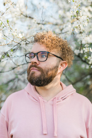 Man with beard and mustache on smiling face near sakura flowers or blooming spring tree. Soft and gentle concept. Bearded man with stylish haircut with flowers on background, close up. Hipster near branch of bloom tree.の写真素材