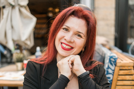 Beautiful happy woman with long red hair enjoying coffee in a street cafeの写真素材