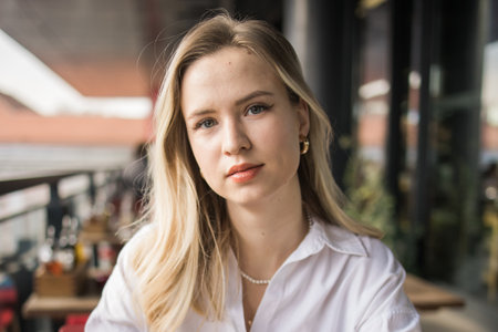 Portrait of beautiful young blonde woman in balcony cafeteria. Happy smiling female relaxing in a...