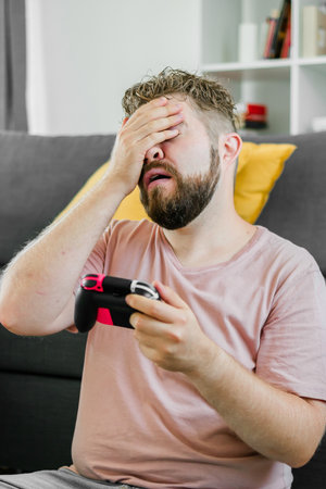 Man spending time at home, sitting on a couch in apartment and playing arcade car video games on...