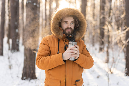 Close-up portrait handsome bearded millennial man in winter clothes and with thermos snow outdoor....