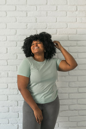 Laughing millennial African American woman with an afro hairstyle and good sense of humor smiling and laugh on brick wall at home background. Copy space. Happiness and good emotions conceptの写真素材