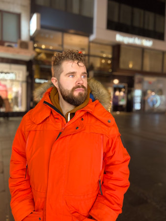 Handsome man model with a hairstyle in winter red jacket walks in night city with festive lights. Christmas and winter holidays seasonの写真素材