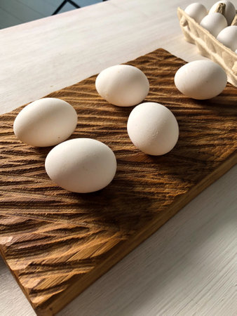 Fresh white eggs arranged on wooden cutting board and in carton box. Rustic and natural protein breakfast ingredients.の写真素材