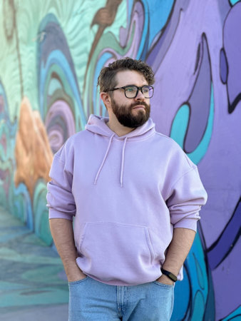 Millennial man in a pastel hoodie standing in front of a vibrant, abstract mural. Soft fabric and bold graffiti creates a striking contrast of modern urban style. Street urban style fashion, creativity individuality, modern art and self-expression conceptの写真素材