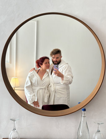 Millennial couple relaxing in hotel robes captured in a round mirror. Cozy moment reflects intimacy and leisure in a tranquil. Spa and wellness hotelの写真素材