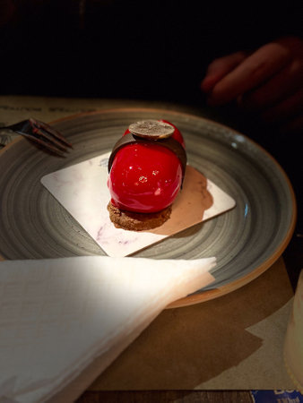 Close-up gourmet dessert with red glaze and chocolate decoration served on a plate, ready to be...