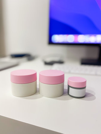 Minimalist desk setup featuring three skincare jars with pink lids, perfectly aligned against a...