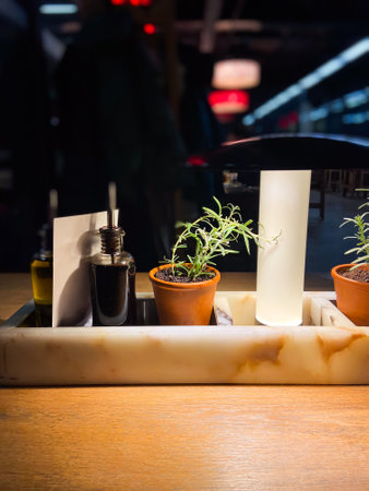 Cozy restaurant table setting with olive oil and balsamic vinegar bottles, flanked by small potted rosemary plants under warm lighting. Blurred background evokes a bustling yet intimate atmosphere, perfect for dining experienceの写真素材