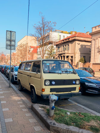 Vintage van car is parked along a bustling city street, surrounded by urban architecture and clear blue skies. Scene captures a blend of nostalgia and everyday life in a lively neighborhoodの写真素材