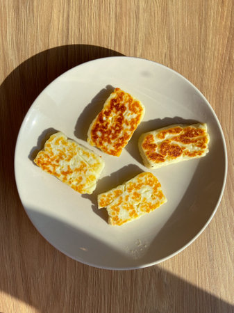 Four pieces of grilled cheese are artfully arranged on a white plate, sitting on a wooden surface...
