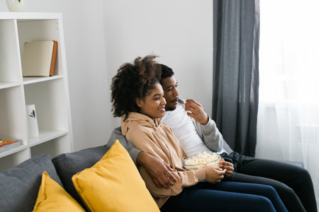 African American couple wife husband watching movie. Family pastime and leisure, watch television,...
