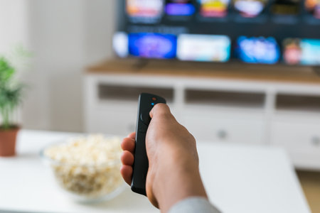 African american woman sits on a gray sofa, enjoying a bowl of popcorn while watching a movie or...