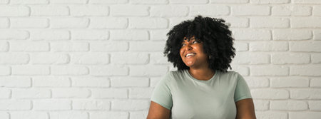 Banner happy stylish African American young woman with Afro hair laughing looking away standing against white brick wall background copy space.の写真素材