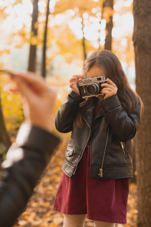 Child taking picture her mother on retro camera in autumn park. Hobbies and leisure concept.の写真素材