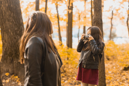 Child taking picture her mother on retro camera in autumn park. Hobbies and leisure concept.の写真素材