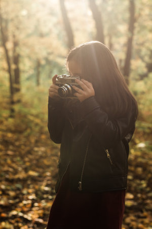 Child girl using an old-fashioned camera in autumn nature. Photographer, fall season and leisure concept.の写真素材